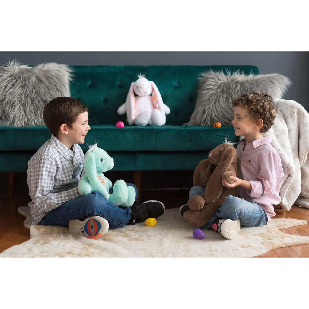two young boys sitting on the floor facing each other and holding two stuffed animal bunnies