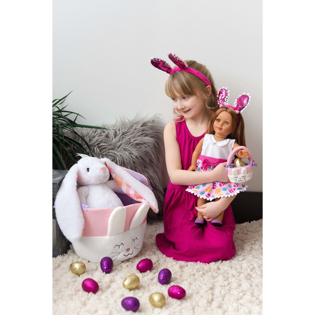 young girl holding doll and looking at a plush bunny sitting in an easter basket